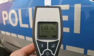 Alkomat w ręce na tle niebieskiego radiowozu policyjnego z napisem "POLIZEI".